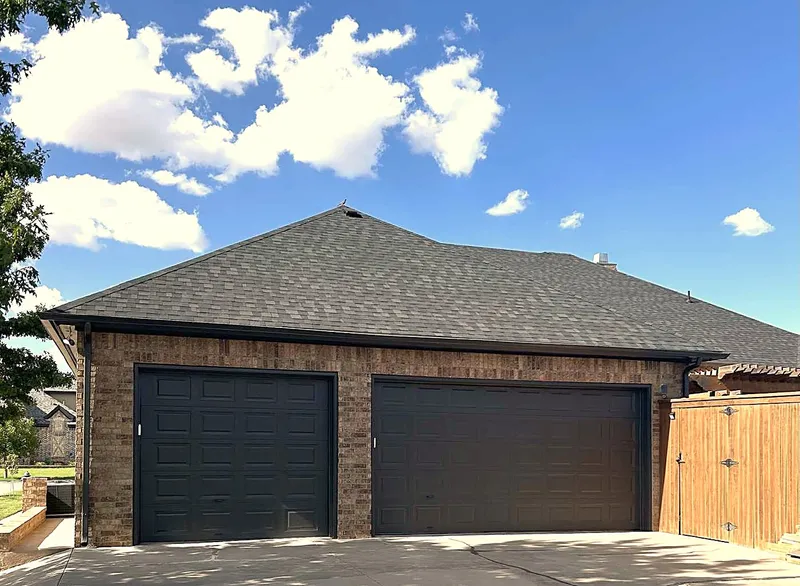 A brick two-car garage with a new dark shingle roof