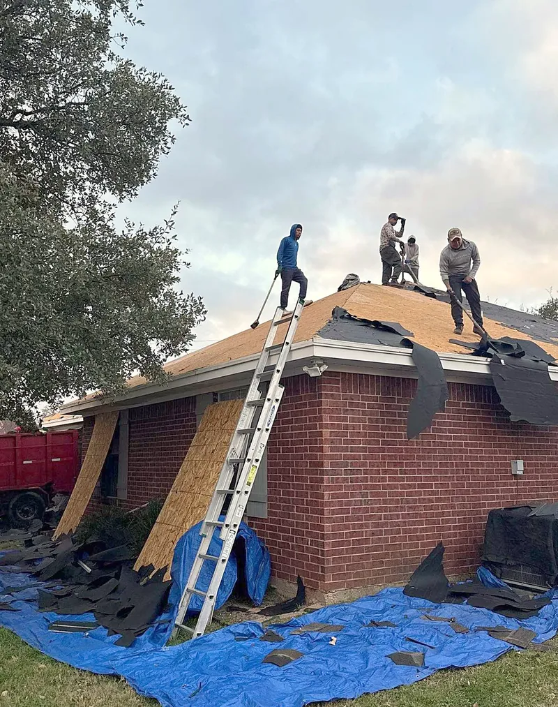 The crew tearing off an old roof on a brick home, with tarps on the ground