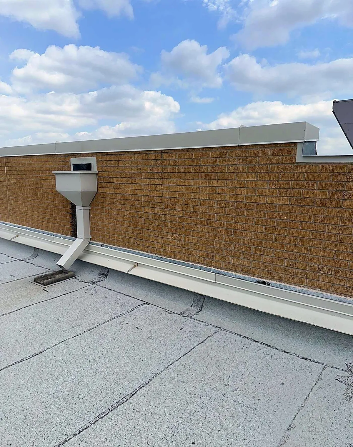 A flat roof with a brick parapet wall and a downspout