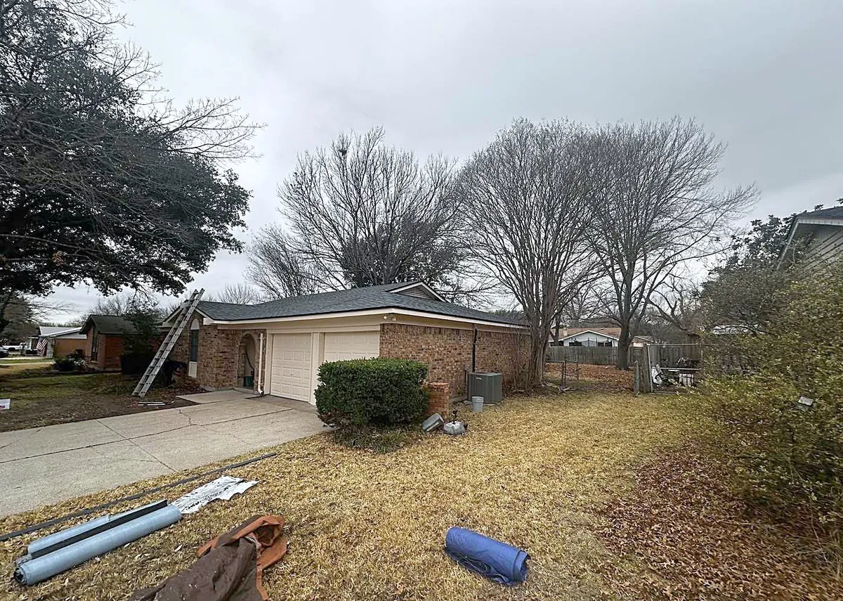 A ladder against a brick ranch home, with roofing materials on the lawn